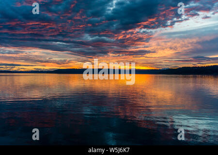 Die Wolken hängen am Himmel, wie die Sonne hinter den Olympic Mountains im Armaturenbrett, Washington. Stockfoto