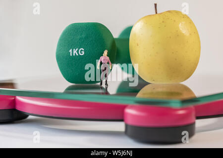 Miniatur Frau Abbildung auf die digitale elektronische Personenwaage, die für das Gewicht des menschlichen Körpers. Frischen Apfel und grün Hanteln in geringer Tiefe Stockfoto