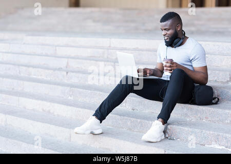 Junge glücklich afrikanischen bärtigen Mann sitzt auf der Treppe mit Laptop Stockfoto