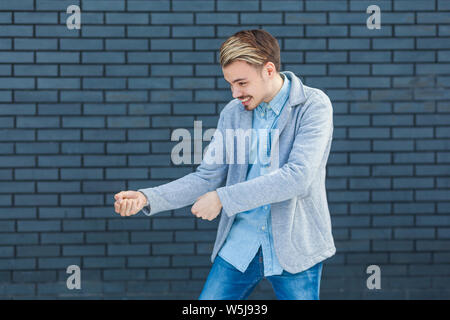 Profil Seitenansicht Portrait von aufmerksamen hübscher junger blonder Mann in lässigen Stil stehen in ziehen Geste oder Boxen angreifen. indoor studio Schuß auf Stockfoto