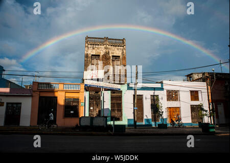 Ein Regenbogen über dem Hotel America in Camguey, Kuba wie Männer fahren mit dem Fahrrad nach einem Regenschauer Stockfoto