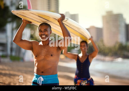 Mitte nach Paar mit einem Surfbrett am Strand. Stockfoto