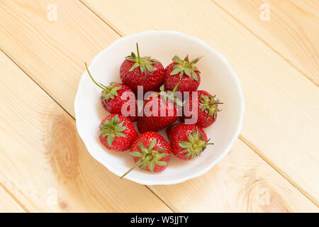 Natürliche süßen Nachtisch. Erdbeeren Ansicht von oben mit der Kopie. Red köstliche Beeren in weiße Schüssel auf hellem Holztisch. Easy Snack für Stockfoto