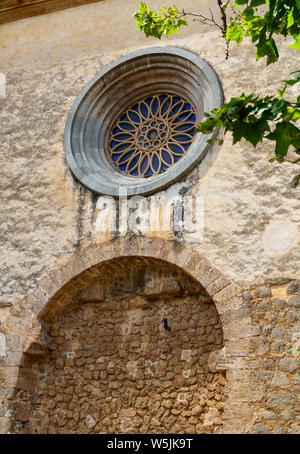 Detail shot der Royal Charter House des Jesus von Nazareth in Valldemossa - grobe Mauer mit einem schönen runden Fenster hinter grünen Blätter Stockfoto