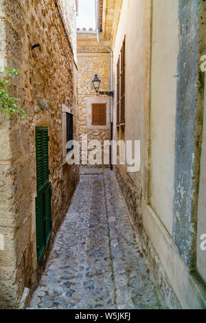 Schmale Gasse mit Kopfsteinpflaster Straße, raue Wände aus Backstein, Geschlossene Fensterläden und einer Laterne führenden Weg von einem überfüllten Piazza in Valldemossa Stockfoto