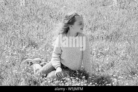 Mädchen sitzt auf Gras an grassplot, grünen Hintergrund. Kind genießen Sie Frühling sonniges Wetter beim Sitzen an der Wiese. Frühling Konzept. Mädchen auf lächelnde Gesicht verbringen Freizeitaktivitäten im Freien. Stockfoto