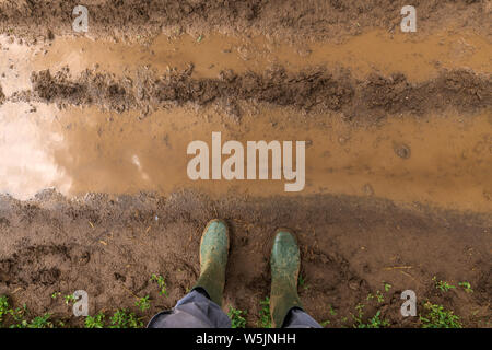 Landwirt in Gummistiefel stehen auf schlammigen Feldweg in der Landschaft, die Füße von oben Stockfoto