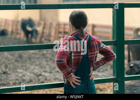 Frau Bauer auf Wasser buffalo Farm. Frau landwirtschaftlichen Arbeitnehmers tragen Plaid Shirt und Jeans bib Overalls auf inländische Wasserbüffel (Bubalus bubalis") Stockfoto