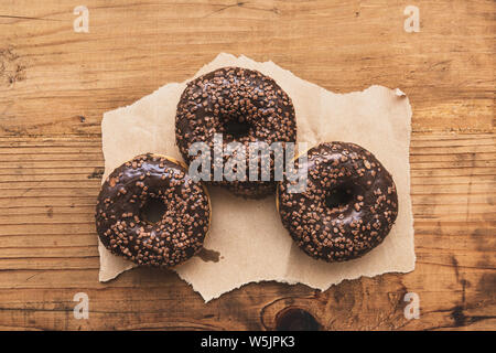 Drei süße Krapfen mit Schokolade und Sahne Krümel auf rustikalen Holztisch, Ansicht von oben Stockfoto