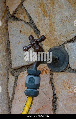 Eine externe tippen oder Wasserhahn mit einem gelben Gartenschlauch für die Bewässerung des Gartens verbunden ist. Stockfoto