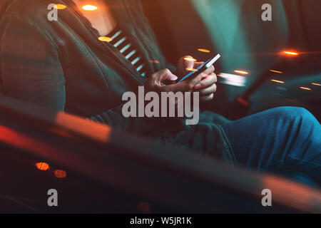 Frau SMS auf Handy im Auto in der Nacht auf einem Parkplatz, Erwachsene weibliche Person mit Smartphone für Kommunikation, selektiven Fokus Stockfoto