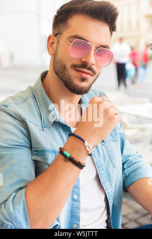 Portrait von attraktiven legerer Mann tragende rote Sonnenbrille am Tisch sitzend in der Stadt lächeln Stockfoto