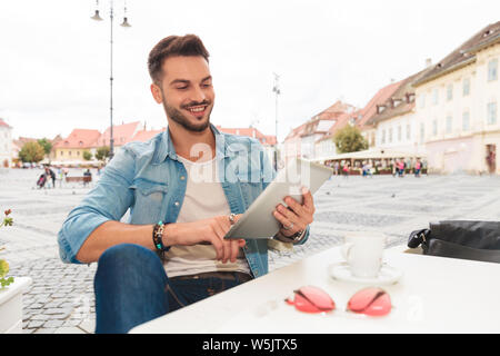 Portrait von lächelnden legerer Mann tippen Tablette auf städtischen Hintergrund während an einem Tisch sitzen Stockfoto