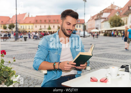 Lächelnd legerer Mann tragen Jeanshemd sitzen am Tisch und Lesen in der Stadt, Porträt Bild Stockfoto