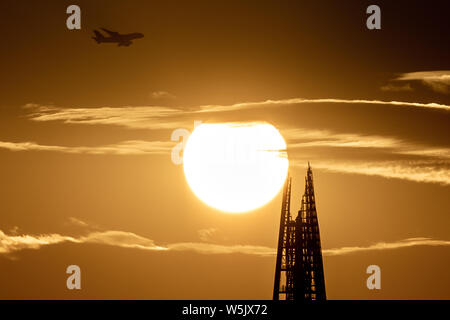 London, Großbritannien. 29. Juli, 2019. UK Wetter: ein Passagierflugzeug auf dem Weg zum London City Flughafen zu landen, Overhead geht in einer dramatischen Sonnenuntergang am Abend über den Shard Hochhaus Gebäude. Credit: Guy Corbishley/Alamy leben Nachrichten Stockfoto