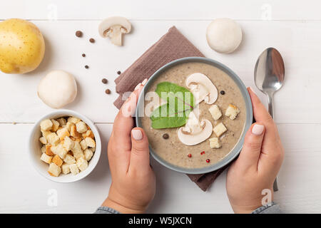 Frauen Hände halten eine graue Schale, Creme von Pilz Suppe auf Licht im Hintergrund. Ansicht von oben, flach Stockfoto