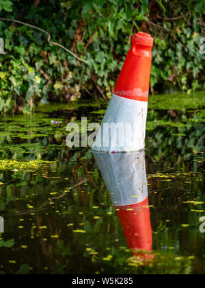 Eine orange Leitkegel im stagnierenden Wasser sitzen. Stockfoto