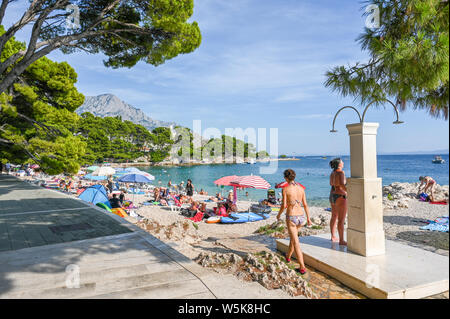 Touristen genießen den Strand von Brela. Die Riviera von Makarska in Kroatien ist bekannt für seine schönen Kiesstränden und kristallklarem Wasser. Stockfoto