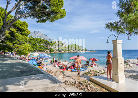 Touristen genießen den Strand von Brela. Die Riviera von Makarska in Kroatien ist bekannt für seine schönen Kiesstränden und kristallklarem Wasser. Stockfoto