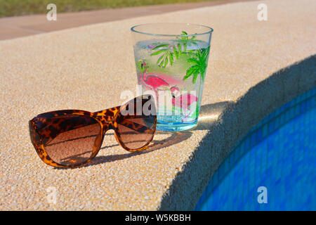 Pool Tag, Sommer Fun Vibes. Paar Kunststoff schildpatt Farbige Sonnenbrille und einem funkelnden kaltes Getränk in einem Plastikbecher am Pool. Stockfoto