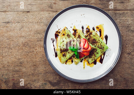 Traditionelle indonesische grüne Pfannkuchen mit Schokolade und Erdbeeren Schichten. Frühstück essen Konzept. Ansicht von oben. Stockfoto