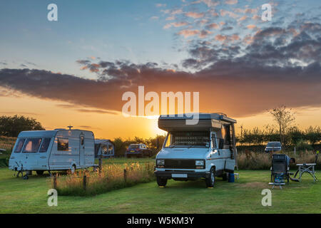 Die Sonne geht hinter einem Wohnmobil auf einem Campingplatz nach einem schönen Sommertag in North Devon. Stockfoto