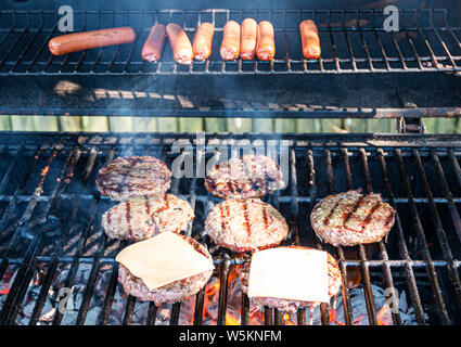 Hot Dogs, Hamburger und Cheeseburger sind Kochen auf dem Grill mit heißen Kohlen darunter. Stockfoto