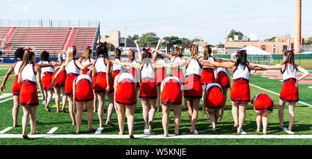 Ein High School Girls kick line Team in roten, weißen und blauen Uniformen üben auf einem Rasenfeld. Stockfoto