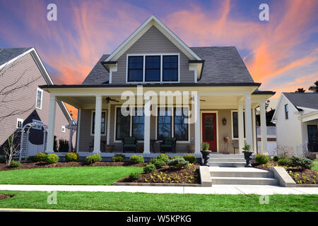Sonnenuntergang hinter einem mit Einlieger Suburban Handwerker Haus mit großer Veranda, weißen Säulen, und eine rote Tür. Stockfoto