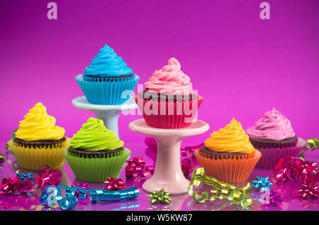 Regenbogenfarbige Frosted Chocolate Cupcakes mit Konfetti und Bögen für eine Partei Stockfoto