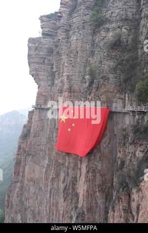 Chinesische Arbeiter hängen einen großen nationalen Flagge der 70. Jahrestag der Gründung der Volksrepublik China entlang einer Klippe zu markieren am Taihang Stockfoto