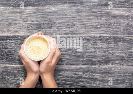 Hand mit einem Styropor Becher heißen Kaffee über holztisch Hintergrund Stockfoto