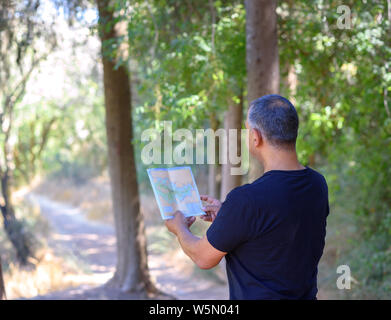 Zurück Seite Reisende ältere Menschen auf der Suche nach rechts Richtung auf der Karte, sonnigen Tag, Reisen entlang der Natur. Alte Tourist mit Karte steht in herrlicher Wald, Freiheit, aktiv bietet ein tolles, glückliches und Gesundheit Ruhestand Stockfoto