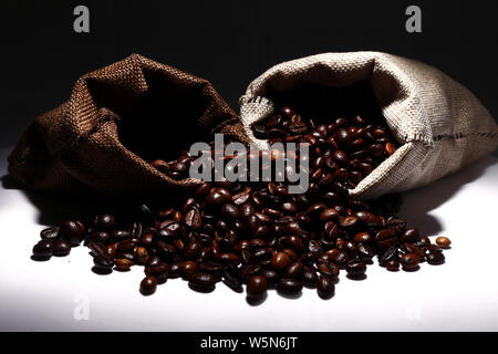 Foto von Kaffee Bohnen verschütten aus Jute Sack oder Beutel Schuß auf weißem Hintergrund Stockfoto