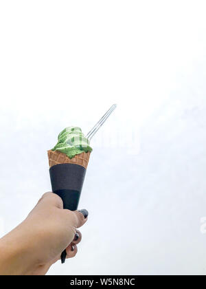 Hand, grüner Tee matcha Eis in den Kegel mit durchsichtigem Kunststoff Löffel auf weißen Raum. Stockfoto