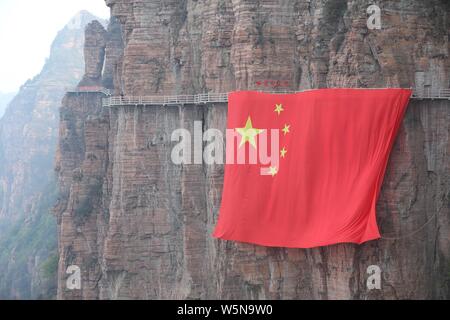 Chinesische Arbeiter hängen einen großen nationalen Flagge der 70. Jahrestag der Gründung der Volksrepublik China entlang einer Klippe zu markieren am Taihang Stockfoto