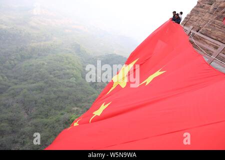 Chinesische Arbeiter hängen einen großen nationalen Flagge der 70. Jahrestag der Gründung der Volksrepublik China entlang einer Klippe zu markieren am Taihang Stockfoto