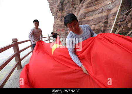 Chinesische Arbeiter hängen einen großen nationalen Flagge der 70. Jahrestag der Gründung der Volksrepublik China entlang einer Klippe zu markieren am Taihang Stockfoto