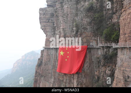 Chinesische Arbeiter hängen einen großen nationalen Flagge der 70. Jahrestag der Gründung der Volksrepublik China entlang einer Klippe zu markieren am Taihang Stockfoto