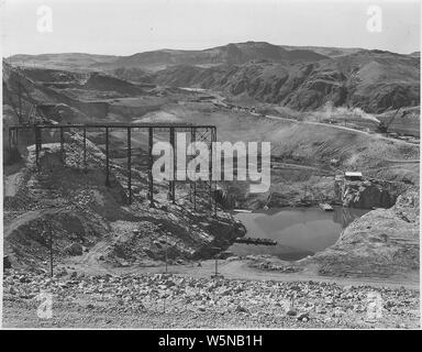 Allgemeine Ansicht der East Pit und forebay Folie mit der Kälteanlage in einem Schuppen auf Rock Vorgebirge und Ausrüstung für das Einfrieren von Rohrleitungen untergebracht, auf der Küstenlinie des Pool unten.; Umfang und Inhalt: Foto aus Band 2 einer Reihe von Fotoalben Dokumentation der Bau des Grand Coulee Dam und die damit verbundenen Arbeiten auf dem Columbia Basin Project. Stockfoto