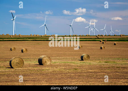 Erneuerbare Energien Windenergieanlagen auf einem abgeernteten Agrarbereich mit Ballen Heu in der kanadischen Prärie von Alberta, Kanada. Stockfoto