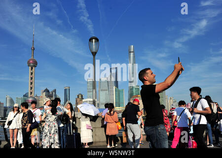 Touristen besuchen die Promenade am Bund entlang des Flusses Huangpu den Oriental Pearl TV Tower zu sehen, links am höchsten, dem Shanghai Tower, rechts am höchsten, Stockfoto