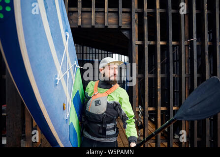 Portrait von bärtigen Athlet im Neoprenanzug holding Surfbrett und Paddel Stockfoto