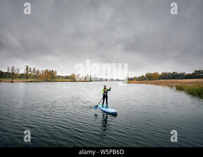 Mann Ausbildung auf dem paddleboard im See gegen bewölkten Himmel Stockfoto