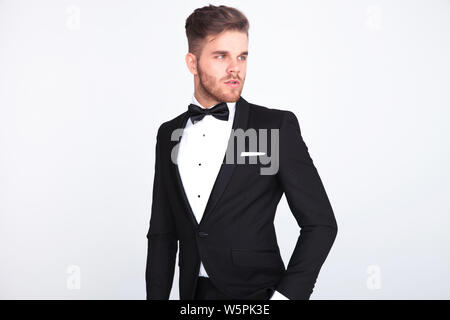 Portrait von stilvollen neugierig Mann mit schwarzen tuxeo und bowtie auf Seite beim Stehen auf hellgrauem Hintergrund Stockfoto