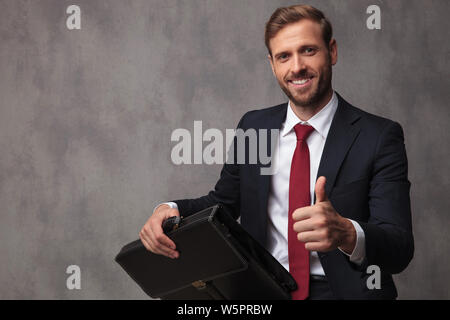 Sitzender Geschäftsmann holding Aktenkoffer macht ok Daumen oben unterzeichnen, studio Bild Stockfoto