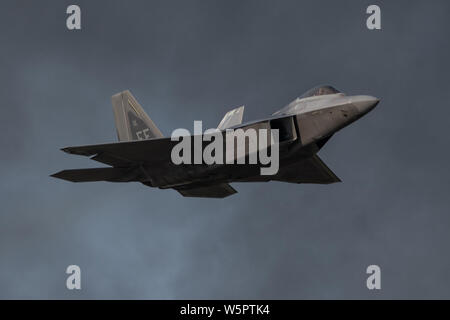 Us Air Force Maj. Paul Lopez, F-22 Demo Team Commander, ergibt sich aus der Verrauchten Himmel nach Durchführung einer High speed pass Manöver bei der EAA AirVenture in Oshkosh, Wis., 28. Juli 2019. Jede F-22 Demonstration dauert ca. 25 Minuten und bietet eine Reihe von Manövern, die die Leistung und Funktionalität von Premier der Welt 5th-generation Fighter. (U.S. Air Force Foto von 2 Leutnant Samuel Eckholm) Stockfoto