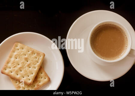Kaffee Tasse und Teller mit Stack von Cream Cracker Kekse isolierten schwarzen Hintergrund. Ansicht von oben. Nahaufnahme Bild. Chinesische Tasse Tee, leckeren Kekse Cookies. Stockfoto