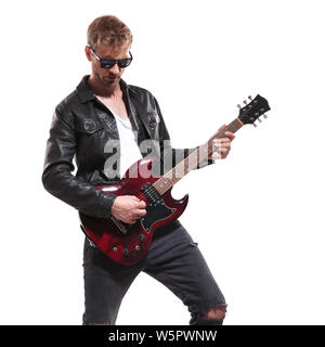 Portrait von Mode Mann mit Lederjacke und Sonnenbrille Spielen seine E-Gitarre beim Stehen auf weißen Hintergrund und nach unten schauen. Stockfoto
