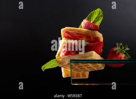 Belgische Waffeln mit Erdbeeren und frischer Minze auf schwarzem Hintergrund. Waffeln auf einem Glas Regal, Ansicht von unten. Kopieren Sie Platz. Stockfoto